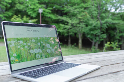 公園の木のテーブルの上に置いたMacbookに「坂や丘のある町 walk along」のホームページが表示されいているところ