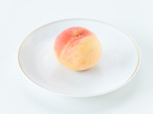 白い陶器の洋皿の上に食べごろの桃がひとつ置いてある