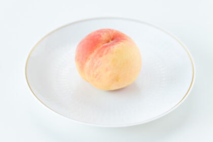 白い陶器の洋皿の上に食べごろの桃がひとつ置いてある