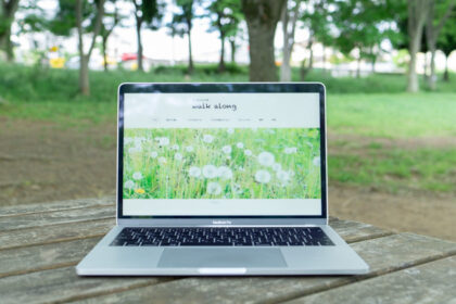 公園の木のテーブルの上に置いたMacbookに「坂や丘のある町 walk along」のホームページが表示されいているところ