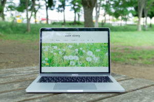 公園の木のテーブルの上に置かれたMacbookに坂や丘のある町 walk alongのトップページが表示されているところ