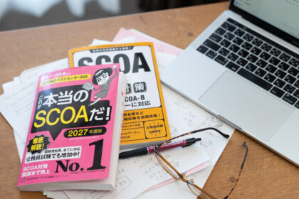 窓際の木製デスクの上に適正検査SCOAの参考書2冊、PCとメガネ、ペンが置いてあるところ